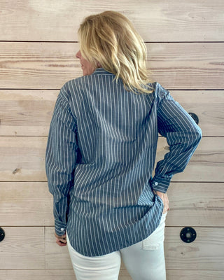 Person wearing a blue striped shirt and white pants against a wooden wall.