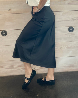 Woman in a white shirt and black skirt standing on a wooden floor.