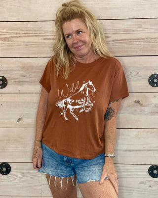Woman wearing a brown t-shirt with a horse graphic against a wooden background