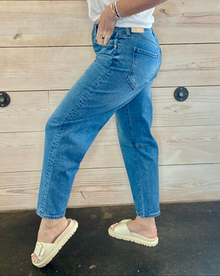 Person wearing blue jeans and a white shirt against a wooden wall.