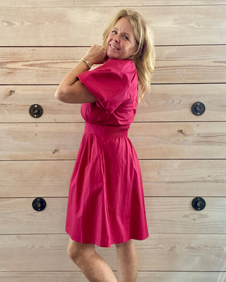 Woman wearing a pink dress standing against a wooden wall.