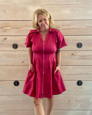 Woman wearing a red dress standing against a wooden wall.