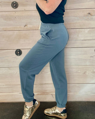 Woman wearing a navy top and light blue pants against a wooden background