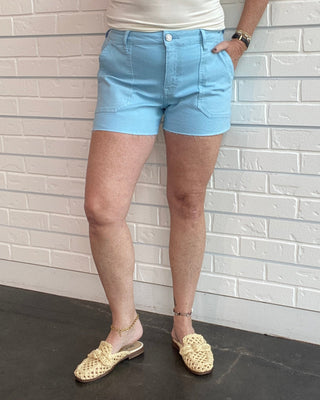 Person wearing a white tank top and light blue shorts standing against a white brick wall.