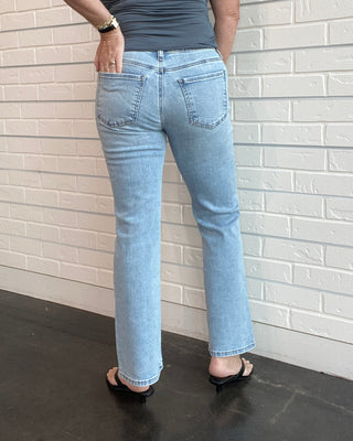 Person wearing a gray tank top and light blue jeans standing against a white brick wall.