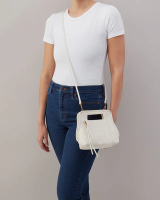Person wearing a white t-shirt and blue jeans holding a white handbag against a plain background