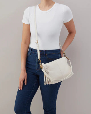 Person wearing a white t-shirt and blue jeans with a beige handbag on a gray background