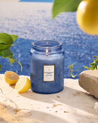 Blue candle with a label on a stone surface near lemons and pool water.