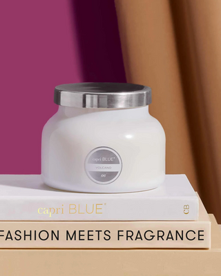 White candle with silver lid on a stack of books, with 'capri BLUE' branding.
