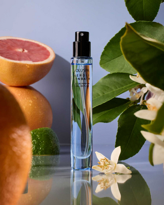 Perfume bottle with citrus fruits and leaves on a reflective surface