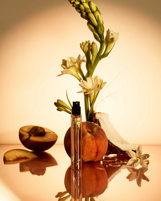 Perfume bottle with flowers and fruit on a reflective surface