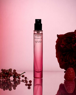 Pink perfume bottle with a red flower and berries on a pink background