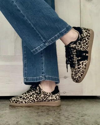 Leopard print sneakers worn with blue jeans on a neutral background