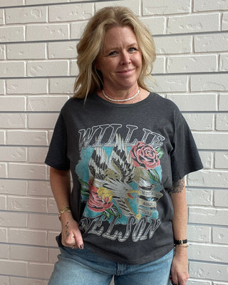 Person wearing a graphic t-shirt and jeans against a white brick wall.