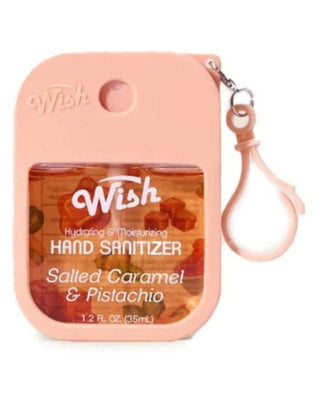 A pink Wish brand hand sanitizer bottle with a matching pink silicone wrist strap, featuring a clear window showing gummy candies inside. The label reads 'Wish Hydrating & Moisturizing Hand Sanitizer Salted Caramel & Pistachio'.