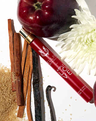 Red lip gloss with cinnamon sticks, apples, and a white flower on a white background