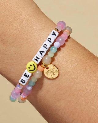 Colorful beaded bracelet with 'BE HAPPY' message on wrist against a beige background