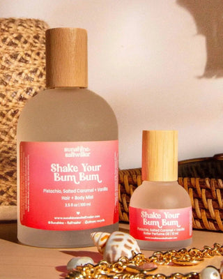 Two bottles of 'Shake Your Bum Bum' product with wooden caps on a textured surface.