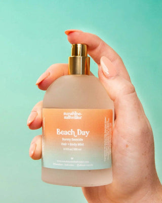 Hand holding a bottle of 'Beach Day' product with a gradient label against a teal background