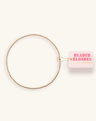 Gold beaded anklet with a pink packaging label on a white background