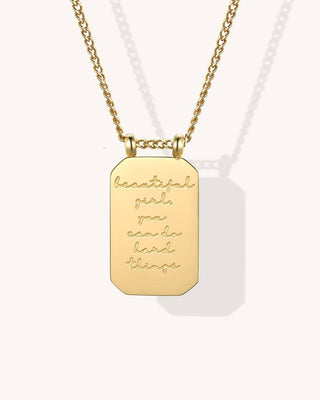 A gold dog tag necklace with a faceted rectangular pendant engraved with the motivational quote 'beautiful girl, you can do hard things', shown on a light cream background.