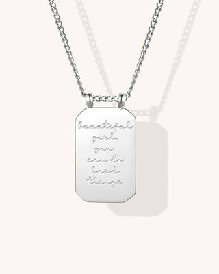 A silver-toned dog tag necklace with an engraved quote that reads 'beautiful girl, you can do hard things' on a light cream background.