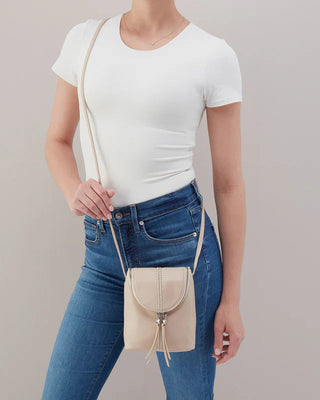 Person wearing a white t-shirt and blue jeans with a beige crossbody bag on a plain background