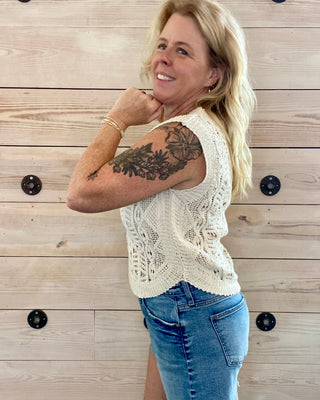 Woman wearing a white lace top and denim shorts against a wooden background