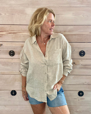 Woman wearing a light-colored shirt and denim shorts standing against a wooden wall.