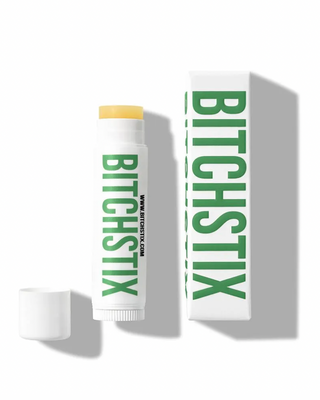 A picture of a Bitchstix lip balm product, with the packaging and the balm itself displayed in front of a white background. The packaging has a green label with 'Bitchstix' written in large letters, and the product is shown to the right of the packaging.