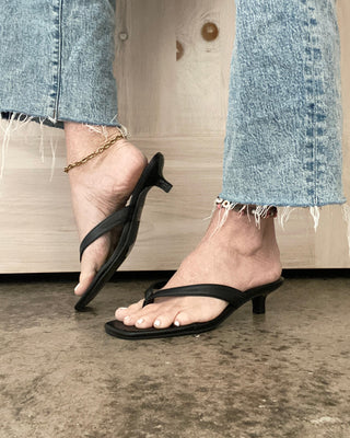 Person wearing black high-heeled sandals with light blue jeans on a neutral background