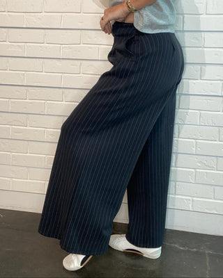 black and grey pinstripe wide-leg pants at Ellipsis Boutique. Pull-on trousers with a pleated front, elastic waist, and soft stretch fabric.