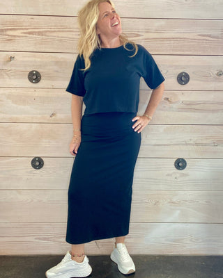 Woman wearing a black outfit standing against a wooden wall.