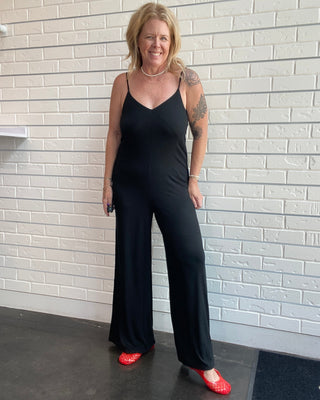 Women's black wide leg jersey jumpsuit with adjustable spaghetti straps, V-neckline, and a relaxed full-length silhouette.