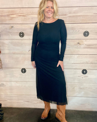 Woman wearing a black dress standing against a wooden wall.