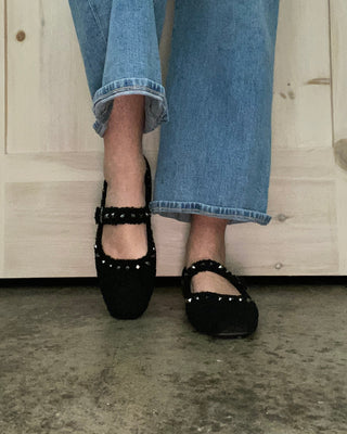 Person wearing blue jeans and black shoes on a wooden floor.