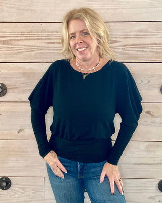 Woman wearing a black top and blue jeans standing against a wooden background
