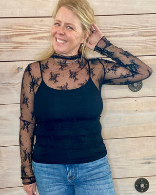 Woman wearing a black lace top and blue jeans against a wooden background