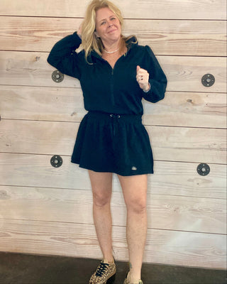 Woman wearing a black outfit against a wooden wall.