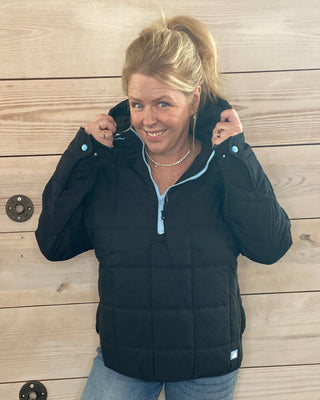 Person wearing a black puffer jacket and blue jeans on a wooden floor.