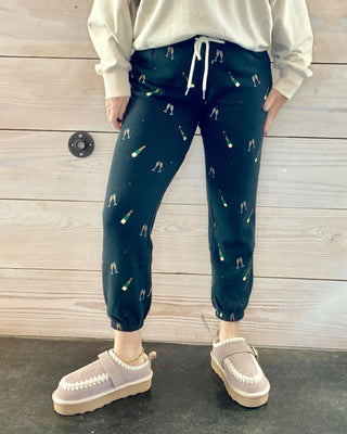 Person wearing a cream sweatshirt and black joggers with champagne pattern against a wooden background