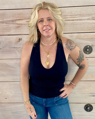 Woman wearing a black tank top and blue jeans standing against a wooden background