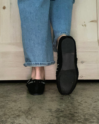 Person wearing black shoes and blue jeans stepping onto a wooden floor from a concrete surface.