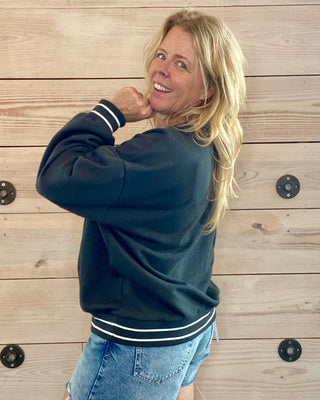Person wearing a black sweatshirt with white trim and denim shorts against a wooden wall.