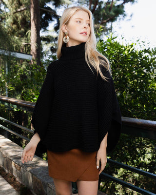 Woman wearing a black turtleneck and brown skirt standing outdoors with greenery in the background