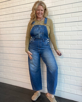 Woman wearing blue denim overalls against a white brick wall