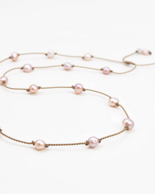 Tula Traveler blush pearls spaced along knotted brown rope, laid on a white background.