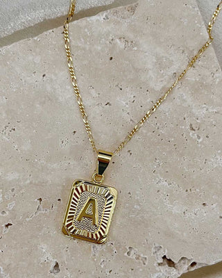 Gold necklace with a pendant featuring the letter 'A' on a stone surface