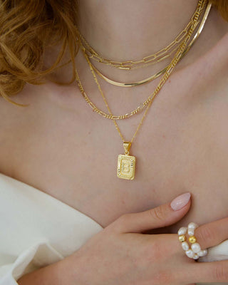 Close-up of a person wearing multiple gold necklaces and a ring with pearls.