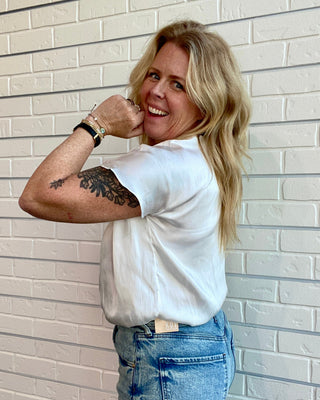 Woman posing against a light brick wall wearing a white t-shirt and blue jeans.